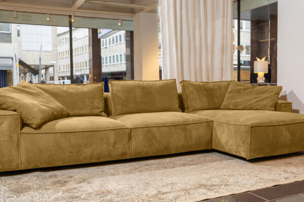 robust-djup-divansoffa-i-senapsgult-manchestertyg-framför-en-vit-gardin